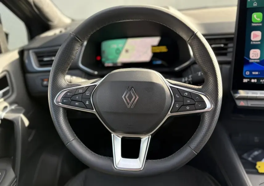 Vue frontale du volant noir perforé de la Renault SYMBIOZ E-Tech 2025 avec commandes intégrées et tableau de bord numérique flou.