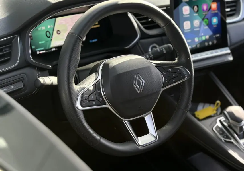 Vue rapprochée du volant noir de la Renault Symbioz 2025 avec commandes intégrées et écran tactile en arrière-plan.