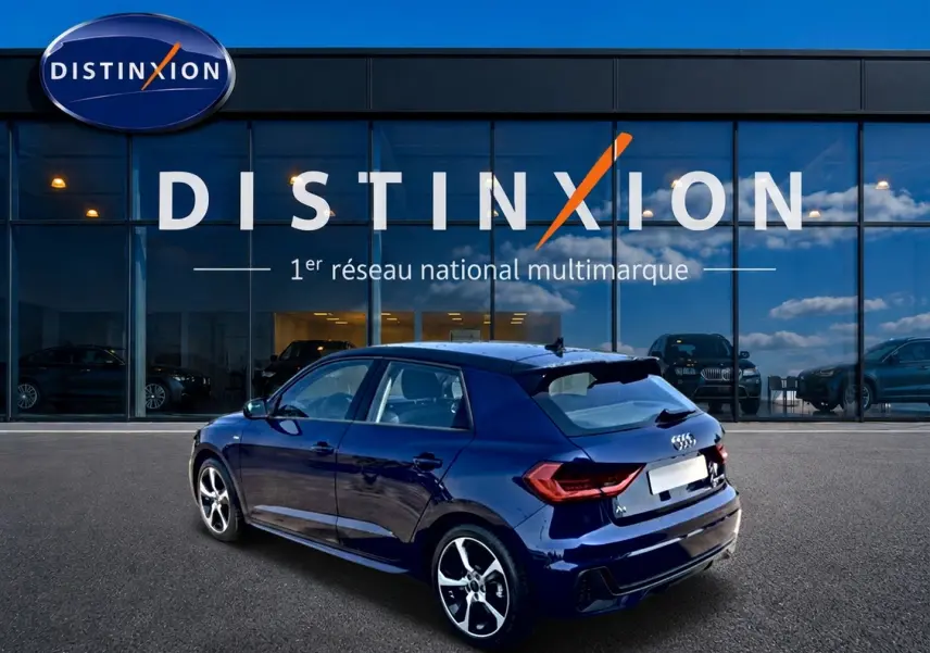 Audi A1 Sportback bleu foncé en 3/4 arrière droit, avec jantes alu et becquet arrière visible devant un showroom Distinxion.
