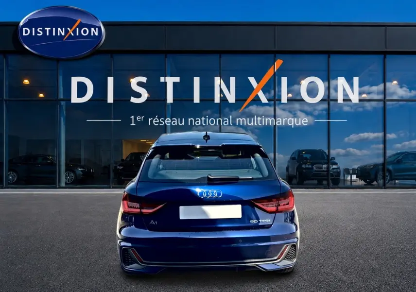 Vue arrière d'une Audi A1 Sportback 30 TFSI bleu foncé, avec feux LED et becquet arrière, devant une vitrine Distinxion.