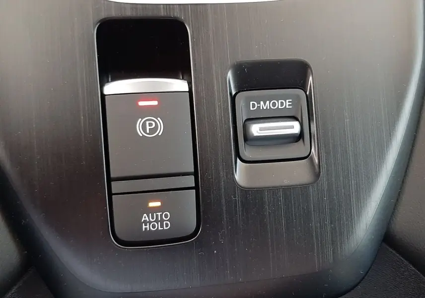 Gros plan sur la console centrale du Nissan Qashqai blanc lunaire 2022, avec boutons frein à main électronique et mode de conduite.