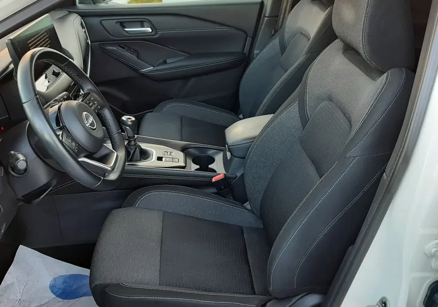 Vue intérieure côté conducteur du Nissan Qashqai blanc lunaire 2022, sièges tissu gris foncé et tableau de bord moderne.