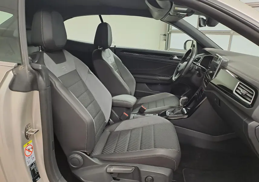 Vue intérieure côté conducteur du Volkswagen T-Roc Cabriolet gris ivoire avec sièges sport R-Line en tissu et alcantara noirs.