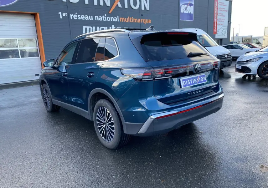 Vue 3/4 arrière droite du Volkswagen Tiguan 1.5 eHybrid bleu nuit métallisé avec jantes stylisées et vitres surteintées.