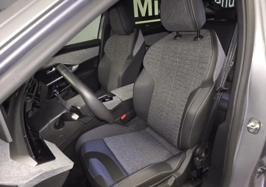 Vue intérieure côté conducteur du Peugeot 3008 gris 2025, sièges tissu gris et cuir noir avec surpiqûres contrastées.