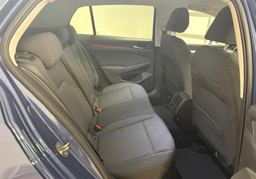 Vue intérieure arrière côté gauche de la Volkswagen Golf 1.5 eTSI 116 DSG7 Bleu Anémone, montrant les sièges arrière et les aérateurs centraux.
