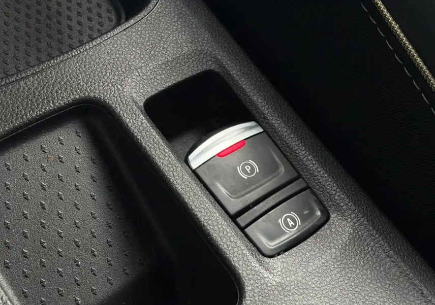 Gros plan sur les commandes du frein de parking électrique et de l’arrêt automatique dans la console centrale noire du Renault Symbioz bleu Iron.