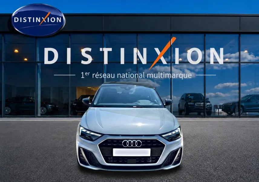 Vue avant d'une Audi A1 Sportback 30 TFSI 116 S line gris arrow avec calandre noire et phares LED devant un showroom Distinxion.