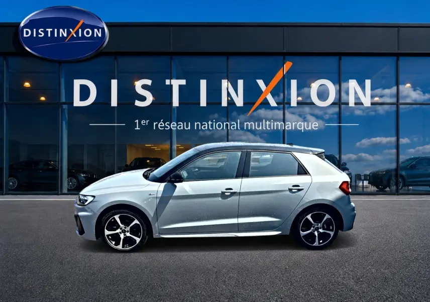 Profil droit d'une Audi A1 Sportback gris arrow avec toit noir, jantes alu et détails S line devant une vitrine Distinxion.