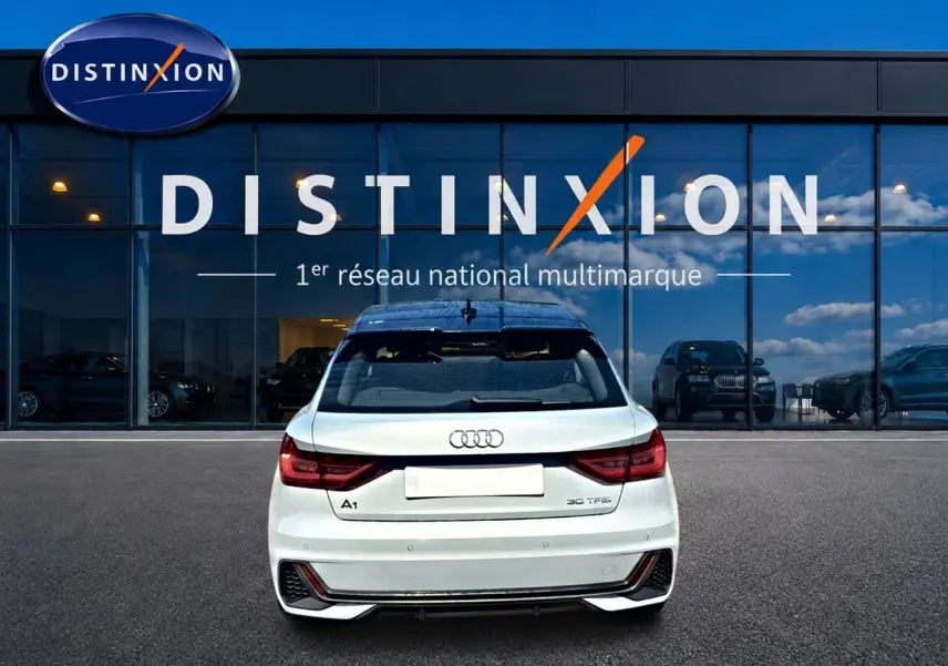 Vue arrière d'une Audi A1 Sportback 30 TFSI gris arrow avec toit noir, stationnée devant une vitrine Distinxion.