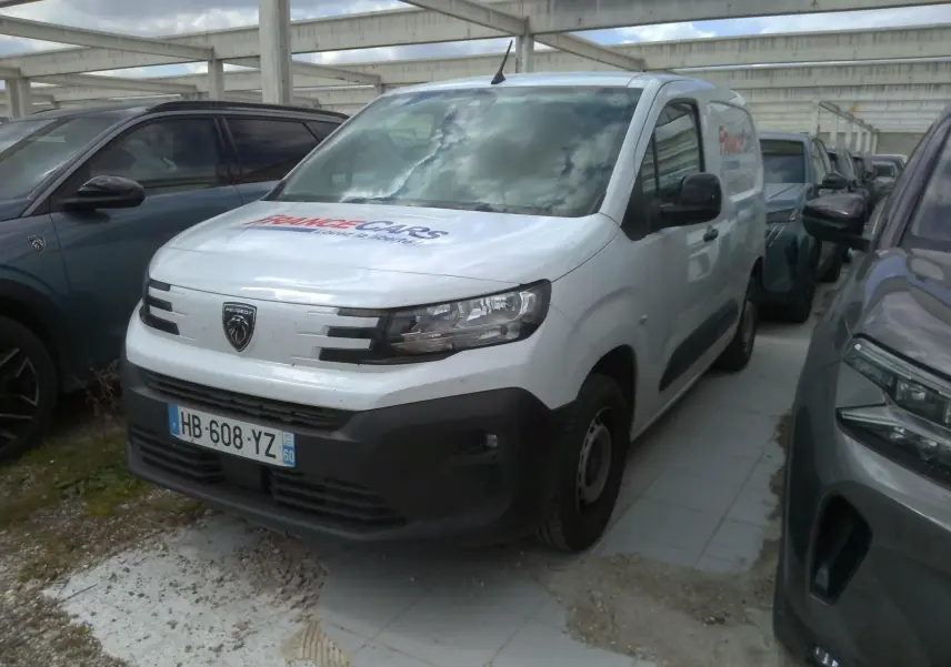Vue 3/4 avant droite d’un Peugeot Partner blanc utilitaire avec logo France Cars sur le capot, stationné entre deux véhicules.