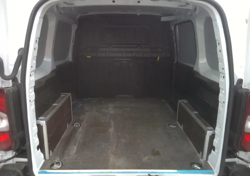 Vue arrière du Peugeot Partner blanc 2025 montrant l'espace de chargement vide avec plancher en bois et parois latérales noires.
