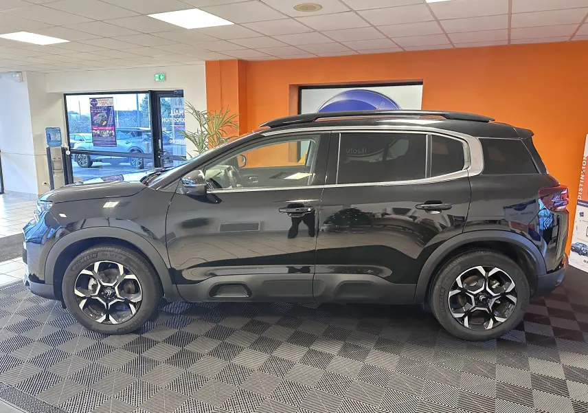 Profil côté gauche d'un Citroën C5 Aircross hybride noir 2025 en showroom, avec jantes alliage biton 18 pouces et vitres surteintées.