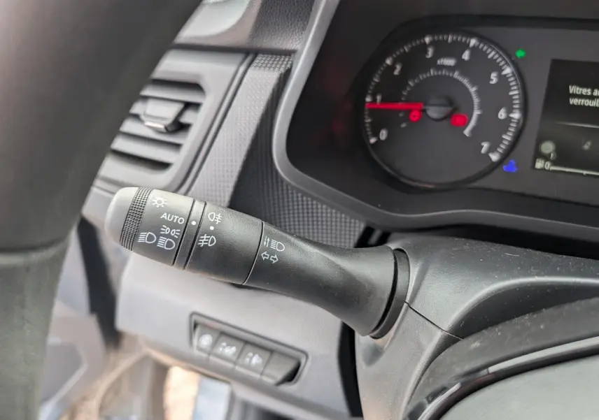Gros plan sur la commande des feux et clignotants à gauche du volant du Renault Trafic Fourgon gris, tableau de bord visible.