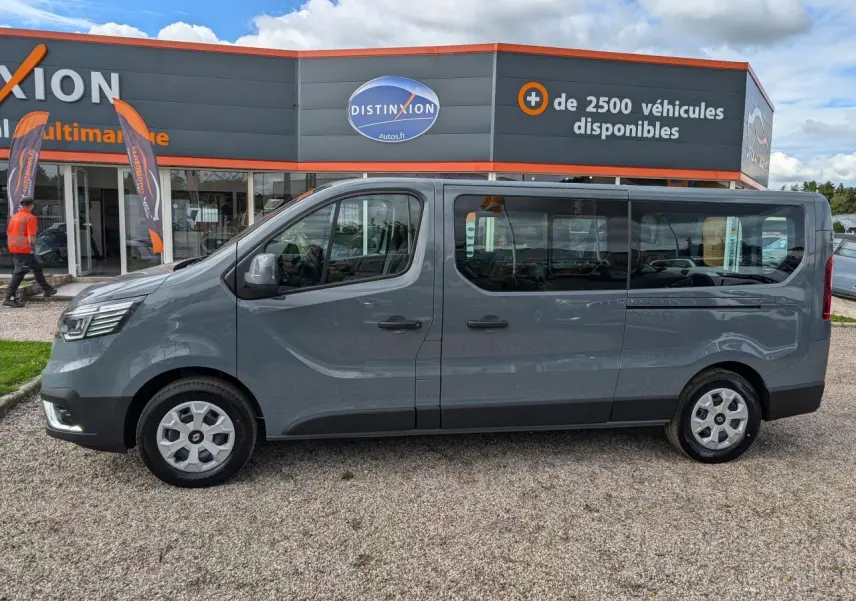 Profil droit du Renault Trafic Fourgon gris, version L2, avec grandes fenêtres latérales et jantes argentées.