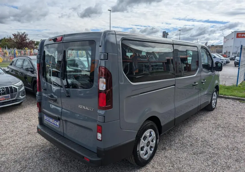 Vue 3/4 arrière droite d’un Renault Trafic Fourgon gris avec vitres latérales et hayon vitré sur un parking.