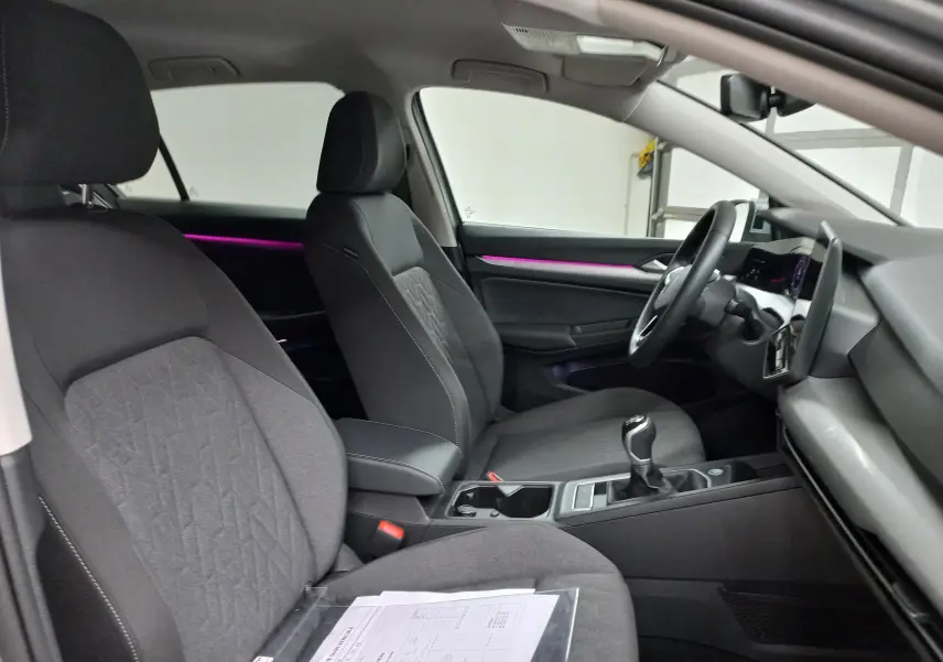 Vue intérieure côté conducteur de la Volkswagen Golf 1.5 eTSI 116 BVM6 avec sièges tissu gris et éclairage d'ambiance violet.