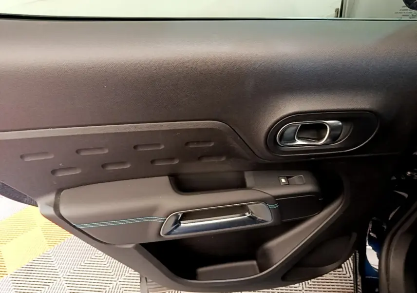 Vue rapprochée de la porte intérieure côté gauche du Citroën C5 Aircross 2023, avec poignée chromée et surpiqûres bleues.