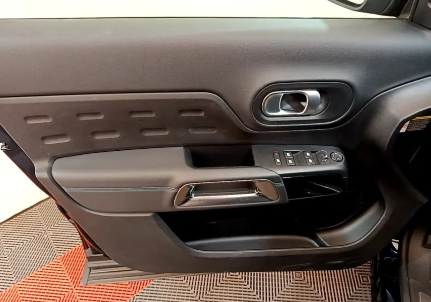 Vue intérieure du panneau de porte avant gauche du Citroën C5 Aircross 2023, avec commandes électriques et poignée chromée.