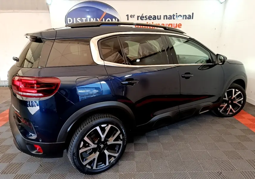 Vue 3/4 arrière droite d’un Citroën C5 Aircross bleu foncé avec jantes alliage et toit noir en intérieur showroom.
