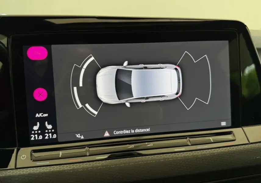 Écran tactile central montrant l’aide au stationnement avec vue aérienne d’une Volkswagen Golf gris clair.