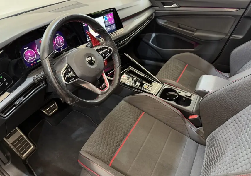 Vue intérieure côté conducteur de la Volkswagen Golf GTI Clubsport 2022, sièges gris avec surpiqûres rouges et tableau de bord digital.