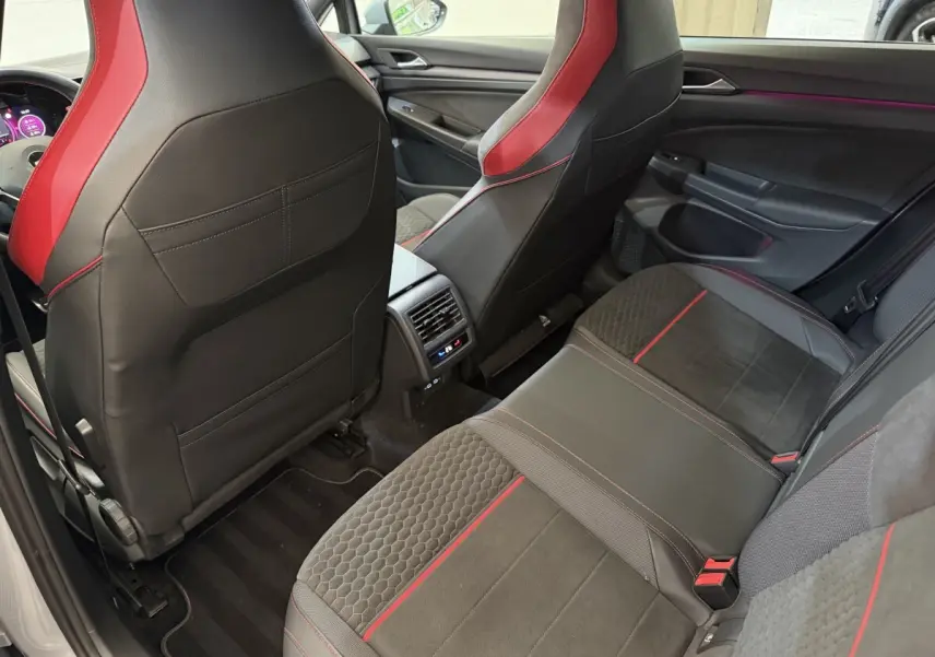 Vue arrière intérieure de la Volkswagen Golf GTI Clubsport 2022, sièges noirs avec surpiqûres rouges et ambiance lumineuse violette.