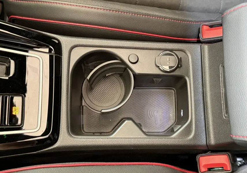 Vue plongeante sur la console centrale noire avec porte-gobelet, recharge sans fil et prise 12V de la Volkswagen Golf GTI gris foncé.
