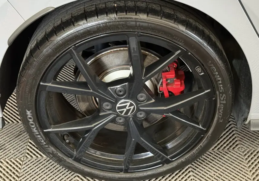 Gros plan sur la roue avant droite noire d'une Volkswagen Golf gris foncé avec étrier de frein rouge visible.