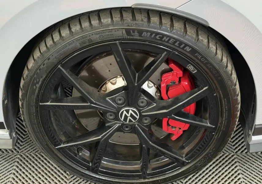 Gros plan sur la roue avant droite noire avec étrier de frein rouge d'une Volkswagen Golf gris foncé.