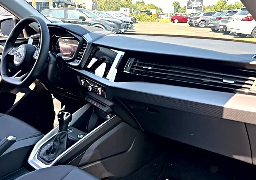 Vue intérieure côté conducteur de l’Audi A1 Sportback 30 TFSI 2026, tableau de bord noir avec écran tactile et volant cuir multifonction.