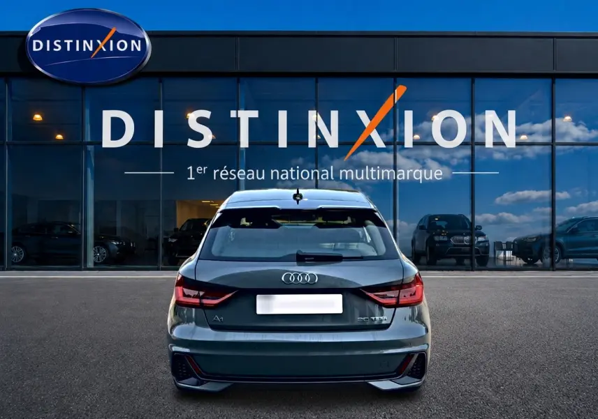 Vue arrière d'une Audi A1 Sportback gris chronos avec feux LED et diffuseur noir, stationnée devant une vitrine Distinxion.
