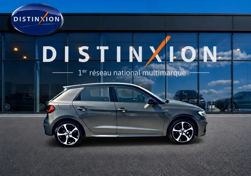Audi A1 Sportback 30 TFSI gris chronos vue de profil côté gauche devant une vitrine avec logo Distinxion.