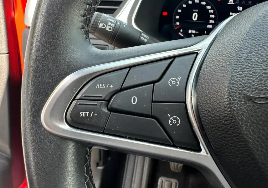 Gros plan sur les commandes du régulateur de vitesse au volant d’un Renault Captur rouge Flamme nacré 2024.