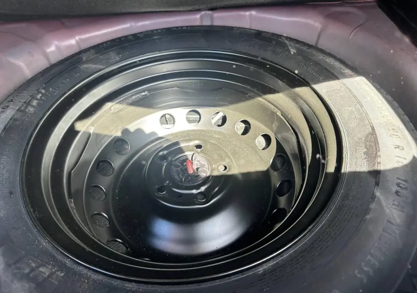 Gros plan sur la roue de secours noire logée dans le coffre d'un Renault Captur 2024 Rouge Flamme nacré.