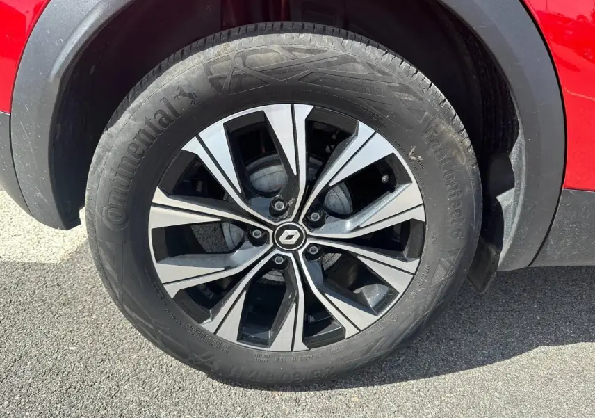 Gros plan sur la roue avant gauche du Renault Captur rouge Flamme nacré avec jante alu bicolore et logo Renault central.