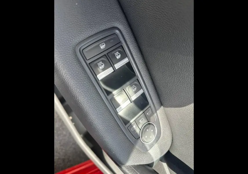 Gros plan sur les commandes de lève-vitres et réglage des rétroviseurs côté conducteur du Renault Captur Rouge Flamme nacré.