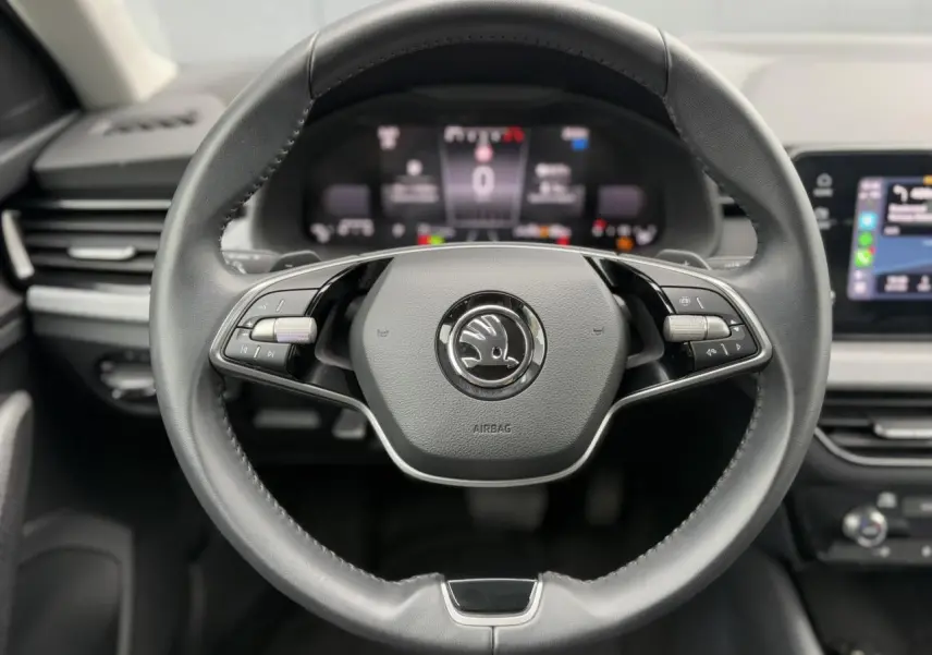 Vue centrée sur le volant cuir multifonctions d'une Skoda Scala 2024, avec tableau de bord numérique flou en arrière-plan.