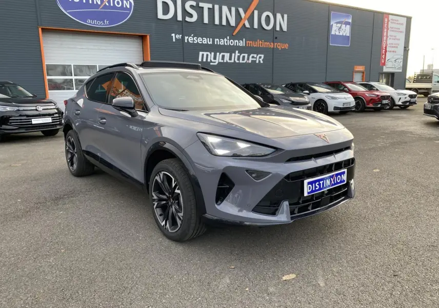 Vue 3/4 avant d’un CUPRA Formentor gris Graphène avec jantes noires et calandre marquée, stationné devant un concessionnaire.