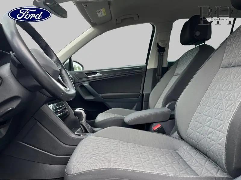 Vue intérieure côté conducteur du Volkswagen Tiguan 1.4 eHybrid 2022 avec sièges tissu gris et accoudoir central.