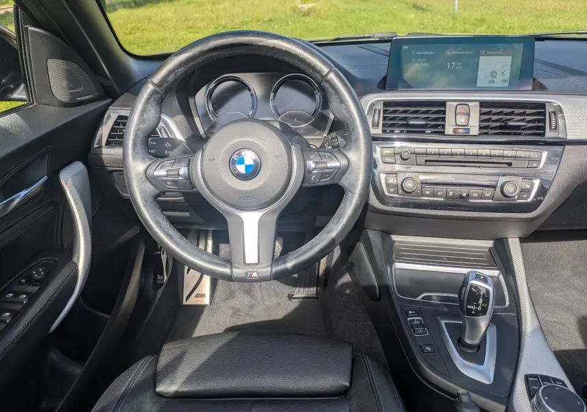 Vue intérieure centrée sur le volant et la console centrale d'une BMW Série 2 Cabriolet noire, avec écran tactile et levier de vitesse automatique.