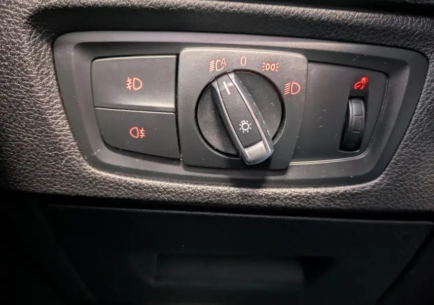 Gros plan sur le bouton de commande des phares et réglage de l’éclairage intérieur dans une BMW Série 2 Cabriolet noire, intérieur cuir noir.