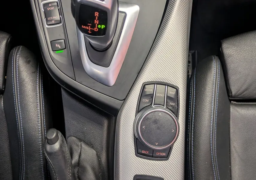 Vue rapprochée de la console centrale d'une BMW Série 2 Cabriolet 218d noire, avec levier de vitesse automatique et commandes multimédia.