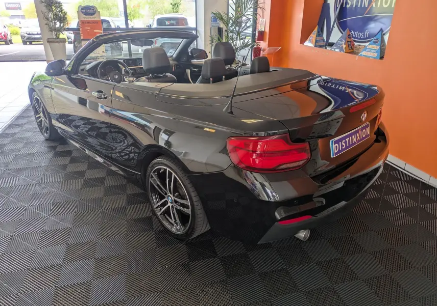 BMW Série 2 Cabriolet 218d Sport noire vue 3/4 arrière droit avec intérieur cuir noir et jantes 18 pouces bicolores.