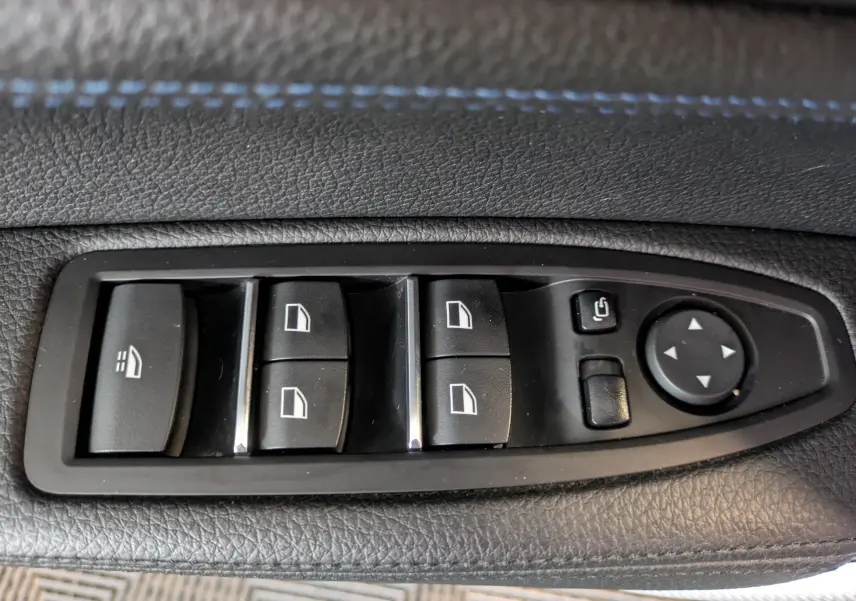 Gros plan sur les commandes de lève-vitres et réglage des rétroviseurs côté conducteur d’une BMW Série 2 Cabriolet noir.