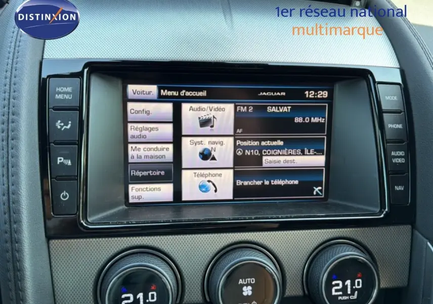 Gros plan sur l’écran tactile central et les commandes de climatisation d’une Jaguar F-TYPE gris, intérieur cuir noir.