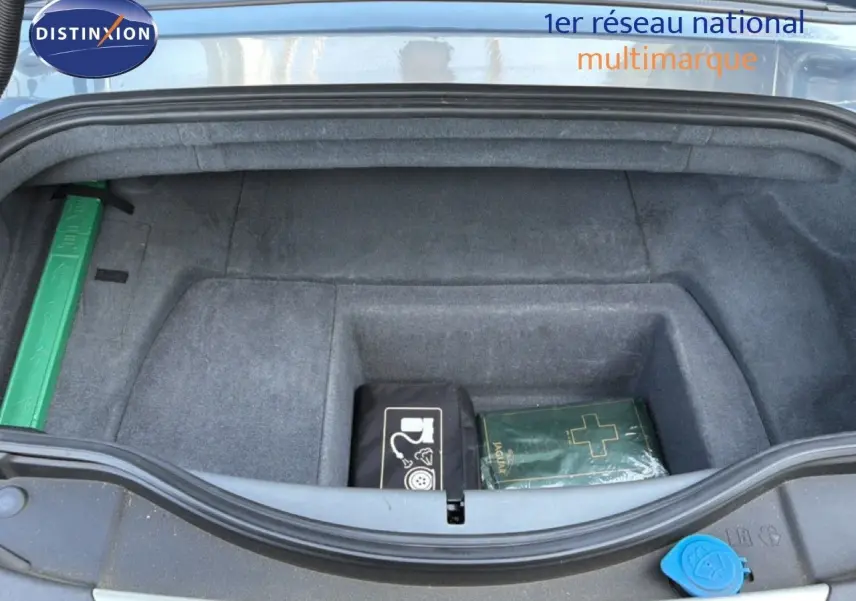 Coffre ouvert d’une Jaguar F-TYPE gris 2013, vue plongeante montrant un rangement avec trousse de secours et kit de réparation.