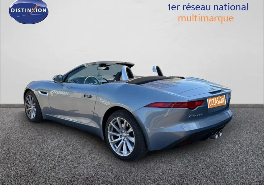 Jaguar F-TYPE cabriolet gris vue 3/4 arrière droit, toit ouvert et jantes alliage visibles.