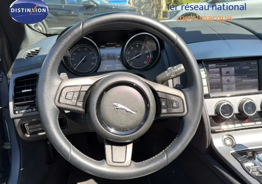 Vue intérieure centrée sur le volant en cuir noir de la Jaguar F-TYPE 3.0 V6, avec tableau de bord et console centrale visibles.