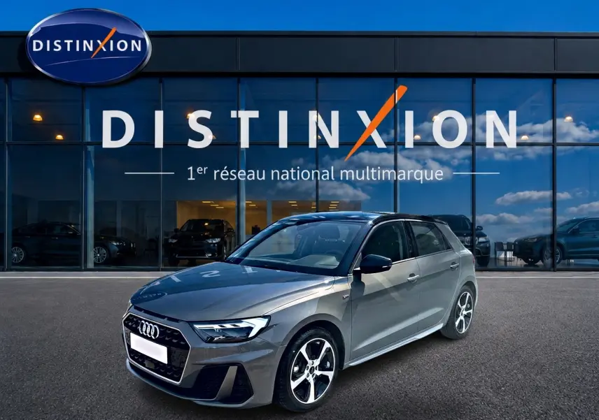 Audi A1 Sportback gris chronos vue 3/4 avant droit avec toit noir et jantes alu distinctives devant un showroom Distinxion.